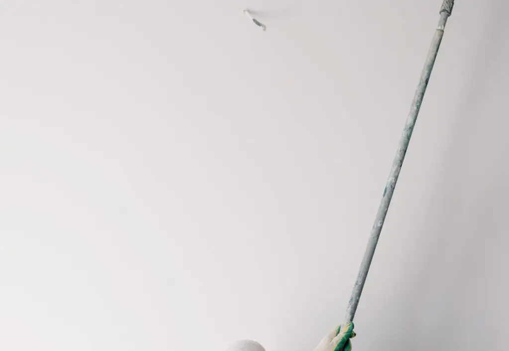 Schilder rolt met een verlengde roller een muur in een lichte ruimte