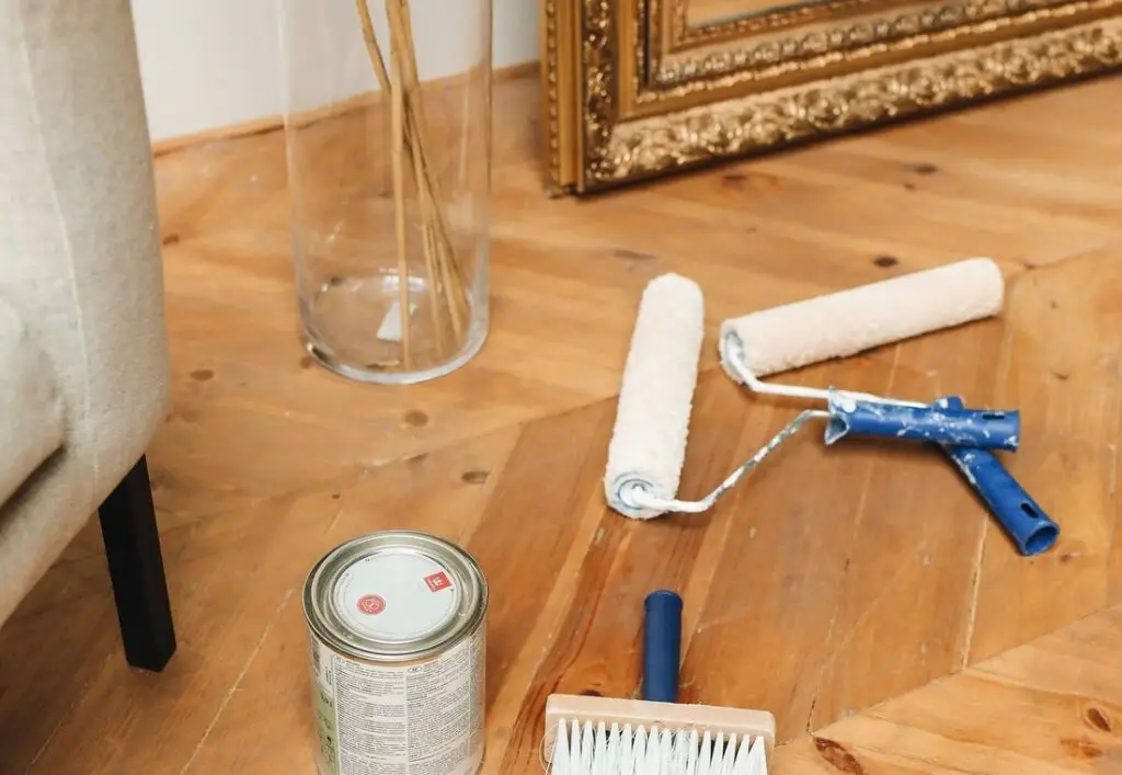 Verfblik, roller en kwast op een houten vloer